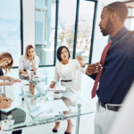 Business team in a modern office engaged in a discussion, with one person presenting and others listening attentively, representing the importance of addressing all three agendas of leadership for holistic, effective leadership.