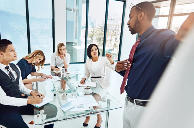 Business team in a modern office engaged in a discussion, with one person presenting and others listening attentively, representing the importance of addressing all three agendas of leadership for holistic, effective leadership.