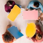 Group of people sitting in a circle holding colourful speech bubbles, symbolising open dialogue, active listening, and the value-building behaviours essential for effective communication.
