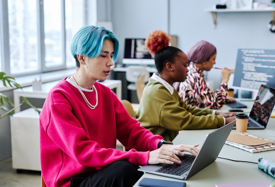 Young professionals from diverse backgrounds working on laptops in a modern office, reflecting the dynamics of leading Gen Y and Z in today’s multigenerational workplace.